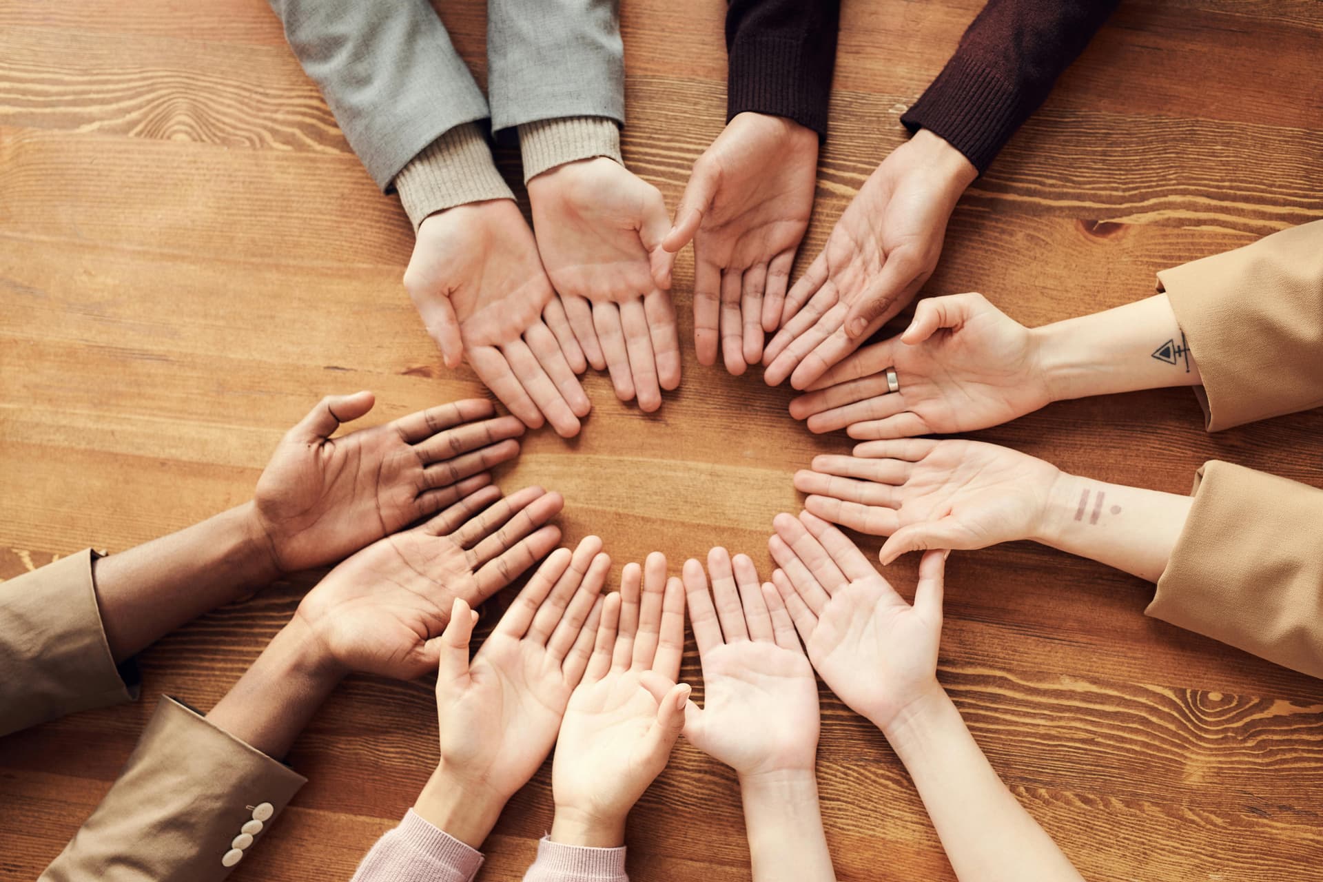Diverse group of hands forming a circle on a wooden table, palms up, symbolizing unity and collaboration.